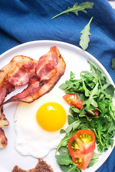 Rejäl hög protein engelsk stil frukost med ägg, stekt bacon och ruccola på plattan. Toppvy, horisontell orientering — Stockfoto