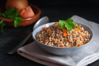 Koyu bir arka plan üzerinde bir kapta havuç, maydanoz ve tereyağı ile Haşlanmış karabuğday tahıl. Koyu arka planda geleneksel Rus yemeği