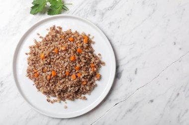 Beyaz taş mermer arka plan üzerinde bir kase havuç, maydanoz ve tereyağı ile Haşlanmış karabuğday tahıl. Kopya alanı ile gri arka plan üzerinde Geleneksel Rus çanak