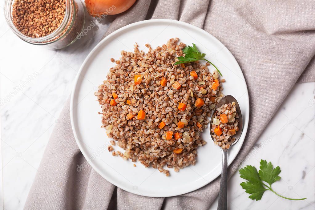 Boiled buckwheat cereal with carrot, parsley and butter in a bowl on a white stone marble background. Traditional Russian dish on gray background with copy space