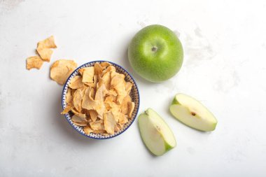 Beyaz bir kapta elma cips ve bir masada bu meyve parçaları