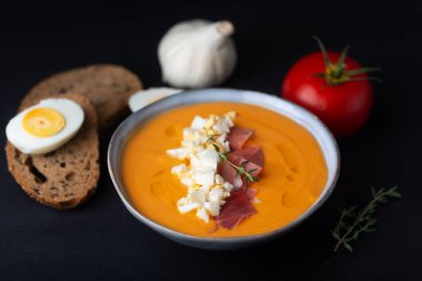 Salmorejo cordobes typical spanish tomato soup similar to the gazpacho, topped with jamon serrano and eggs, black background clipart