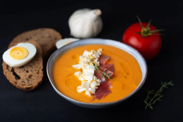 Salmorejo cordobes typical spanish tomato soup similar to the gazpacho, topped with jamon serrano and eggs, black background — Stock Photo, Image