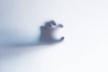 Defocused scary ghost hands behind a white glass background clipart