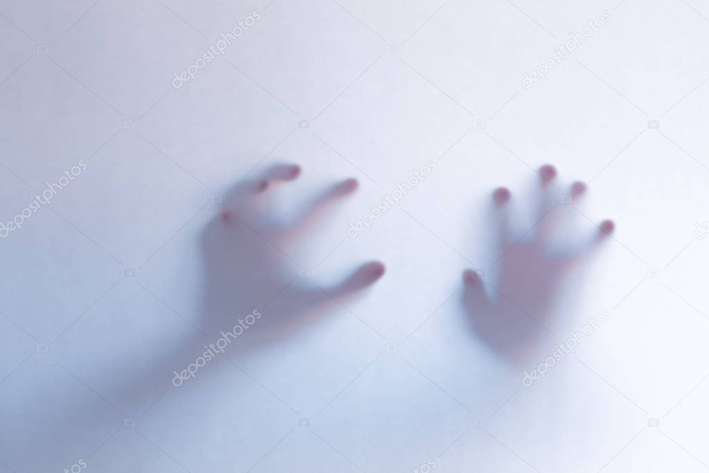 Defocused scary ghost hands behind a white glass background