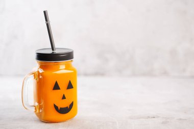 Gri bir arka plan üzerinde korkutucu yüzü ile cam kavanozda Halloween sağlıklı kabak veya havuç içecek