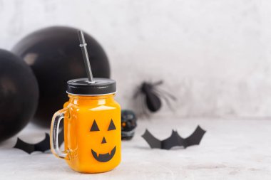 Gri bir arka plan üzerinde korkutucu yüzü ile cam kavanozda Halloween sağlıklı kabak veya havuç içecek