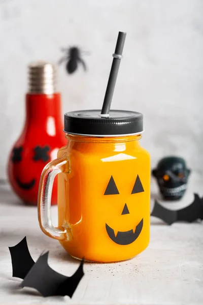 Halloween healthy pumpkin or carrot and tomato drinks in the glass jar with scary face on a gray background