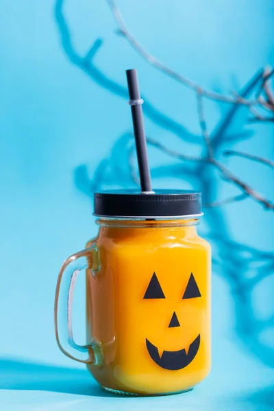Halloween healthy pumpkin or carrot and tomato drinks in the glass jar with scary face on a blue background