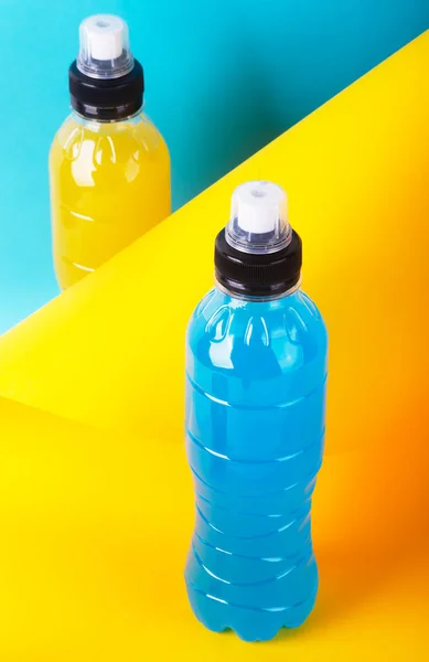 Bebida energética isotónica. Garrafas com líquido transparente azul e amarelo, bebida esportiva em um fundo colorido — Fotografia de Stock