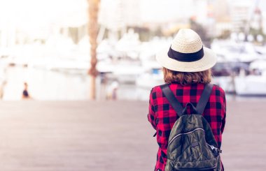 Sırt çantası olan genç bir kadın, Alicante limanının yanında sırtıyla duruyor.