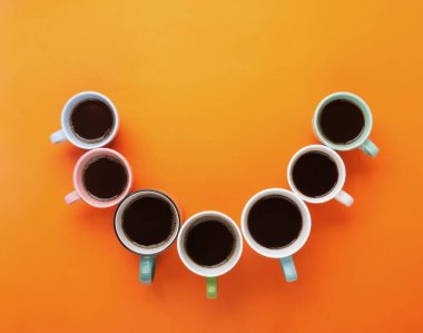 Coffee in the different cups on the bright orange background looks like a smile. Flatlay, cheerful day concept