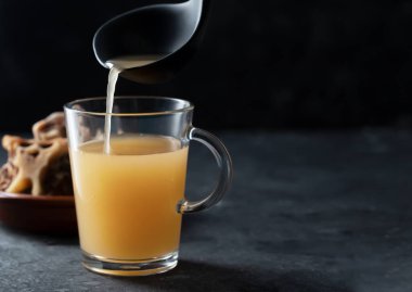 Siyah arka planda cam kavanozda ev yapımı sığır eti çorbası. Kemikler, vücuda proteinlerin yapı taşları olan amino asitleri sağlayan kolajen içerir.