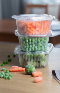 Frozen vegetables green peas in the storage box on the kitchen table, vertical orientation. Freezing is a safe method to increase the shelf life of nutritious foods clipart