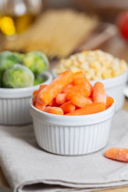 Frozen vegetables such as baby carrot and Brussels sprouts in the bowls on the kitchen table. Freezing is a safe method to increase the shelf life of nutritious foods clipart