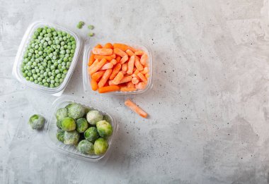 Frozen vegetables such as green peas, brussels sprouts and baby carrot in the storage boxes on the concrete gray background, top view with copy space clipart