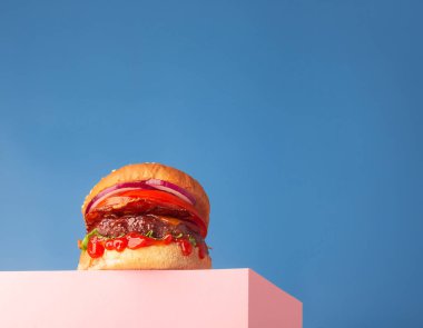 Pembe standa ve mavi arka planda taze sulu etli hamburger. Metin, trend kahraman görünümü ve yatay görünümü için alanı kopyala
