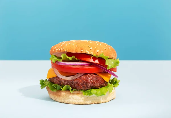 創造的な青の背景に配置された新鮮なジューシーな牛肉のハンバーガー — ストック写真