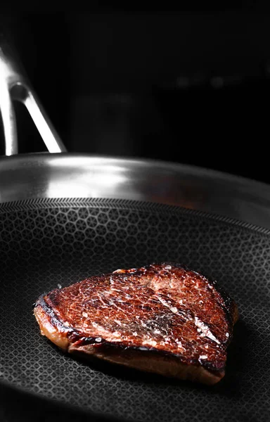 Стейк говядины готовится на темной сковороде — стоковое фото