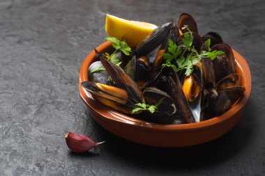Limonlu ve maydanozlu haşlanmış midyeler koyu arkaplanda, yakın plan.