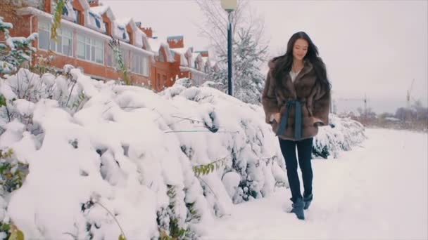 Mujer morena en abrigo de piel sonriendo en el fondo de los edificios en la calle de invierno. cámara lenta — Vídeo de stock