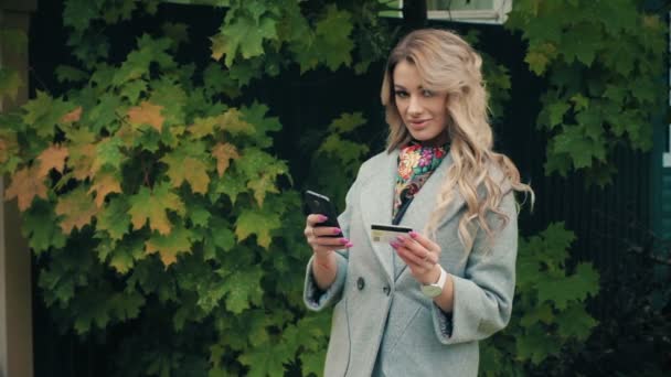 Blond dziewczyna ze smartfonem i kartą kredytową robią zakupy — Wideo stockowe