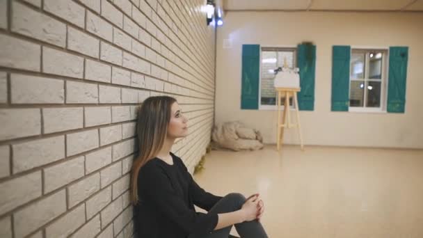 Fille avec et les cheveux bruns s'asseoir appuyé contre le mur de briques . — Video