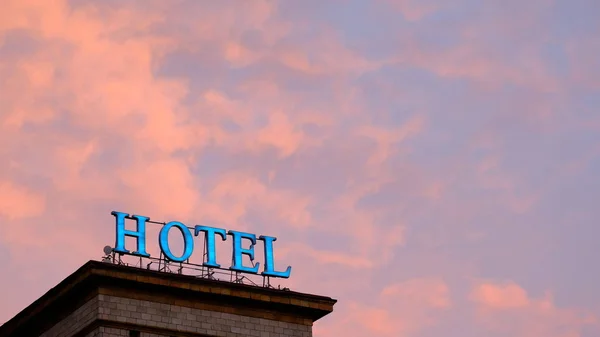 Weathered e queimado neon hotel sinal iluminado contra um colorido e dramático céu vermelho e laranja ao pôr do sol em Nova York — Fotografia de Stock