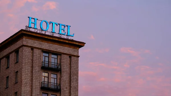 Yıpranmış ve yanmış neon otel işareti New York'ta gün batımında renkli ve dramatik kırmızı ve turuncu gökyüzüne karşı aydınlatılmış