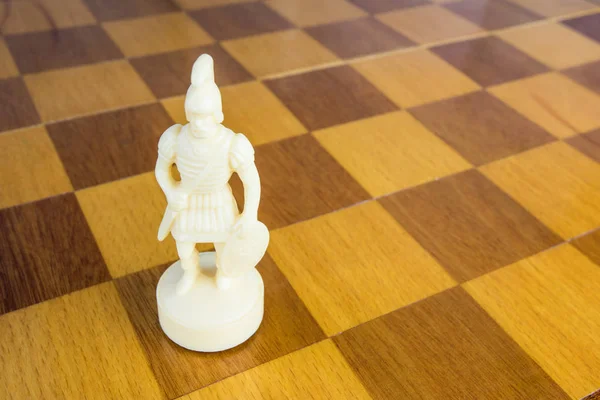 The isolated white chess bishop of stone or plastic on the square wood board