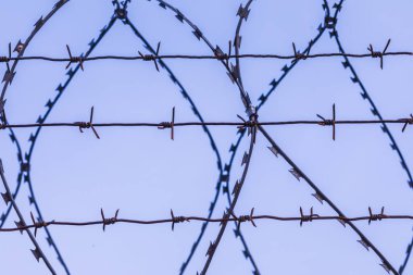 Mavi gökyüzünün arka planındaki dikenli tel silueti.