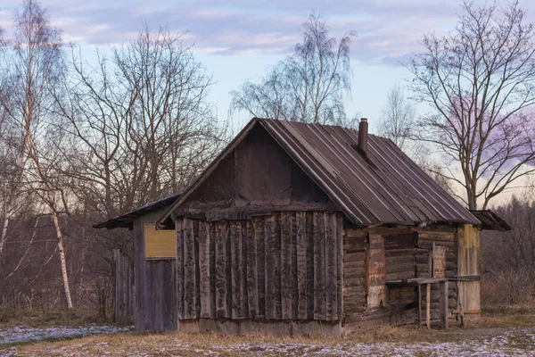 The alone old wood building in the countryside or village with the trees on the background of blue cloudy sky