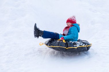 Kırmızı şapka ve atkı tepeden inen mavi giysili kızı siyah kauçuk halka kızak yerine bir kar ile kaplı. Kış resmi tatil eğlence