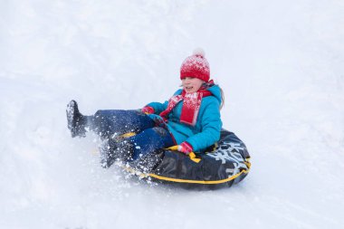 Kırmızı şapka ve atkı tepeden inen mavi giysili kızı siyah kauçuk halka kızak yerine bir kar ile kaplı. Kış resmi tatil eğlence