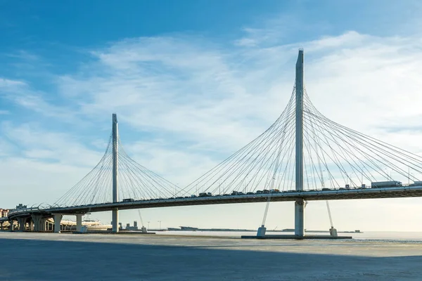 The bridge of circle highway road over Neva river near the mouth of it in the clear day. The winter landscape of the river covered with ice and snow and with the sky with clouds