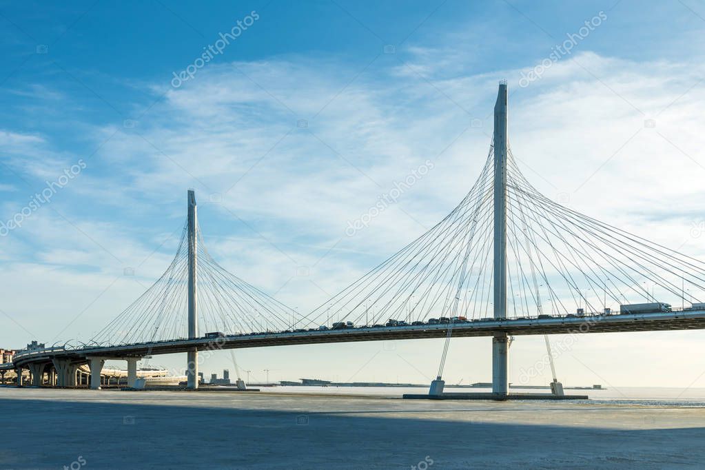 The bridge of circle highway road over Neva river near the mouth of it in the clear day. The winter landscape of the river covered with ice and snow and with the sky with clouds