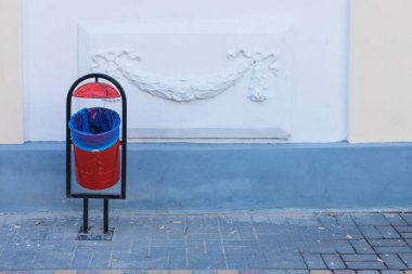 Güneşli yaz gününde süs ile beyaz duvar arka planda şehir veya şehir kaldırım üzerinde kırmızı ve siyah çöp kutusu