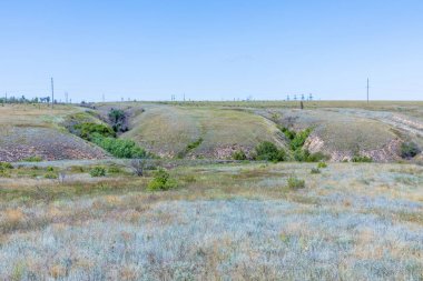 Güneşli yaz gününde Volgograd kenti yakınlarında vadiler ve mavi gökyüzü ile Rus bozkır veya bozkır. Kırsal manzara veya çim, çalılık ve küçük ağaçlar ile elektrik hatları veya şebeke ile görünümü 