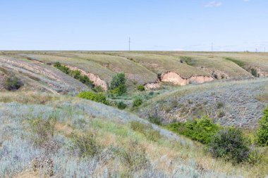 Güneşli yaz gününde Volgograd kenti yakınlarında vadiler ve mavi gökyüzü ile Rus bozkır veya bozkır. Kırsal manzara veya çim, çalılık ve küçük ağaçlar ile elektrik hatları veya şebeke ile görünümü 