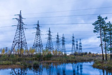 Sonbahar kırsal kesimlerinde kabloları olan elektrik kuleleri bulutlu mavi gökyüzünün arka planında bataklık ve orman. 