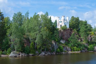Eski yalnız kale, küçük kale, deniz feneri ya da deniz feneri ya da dağın tepesindeki yeşil kale ile okyanus, deniz, göl suyu arasında açık güneşli yaz günlerinde dalgalar