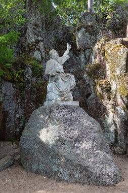 Güneşli yaz günlerinde ormanda yeşil yosun ve yosunla kaplı, elleri dağların ya da kayalıkların arasında yükselen yaşlı bir adamın anıtı ya da anıtı.