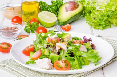 Beyaz ahşap zemin üzerinde bir tabakta tavuk, avokado, domates ve keten tohumu ile taze salata. Sağlıklı gıda.