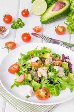 Beyaz ahşap zemin üzerinde bir tabakta tavuk, avokado, domates ve keten tohumu ile taze salata. Sağlıklı gıda.