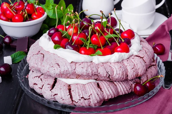 Chocolate Pavlova cake with whipped cream and cherries on a black wooden background