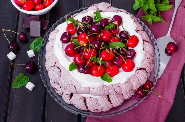 Chocolate Pavlova cake with whipped cream and cherries on a black wooden background