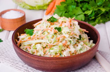 Beyaz ahşap zemin üzerinde kase taze lahana salatası.