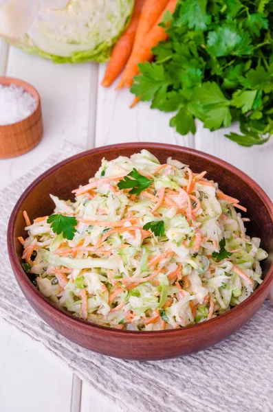 Beyaz ahşap zemin üzerinde kase taze lahana salatası.