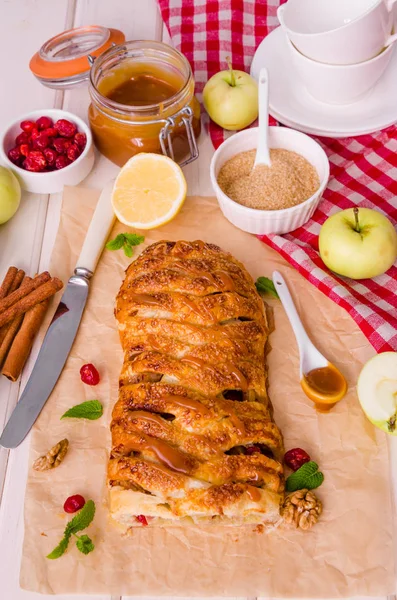 apple pie with dried cherries, walnuts, lemon zest and cinnamon on white wooden background