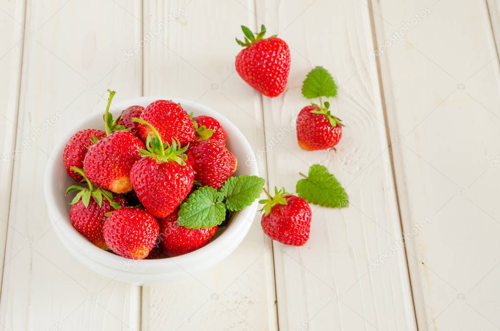 Fresh ripe strawberries in a bowl on a white wooden background.
